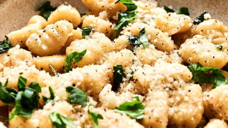 Close-up of a plate of gnocchi topped with grated cheese, freshly ground black pepper, and chopped parsley.