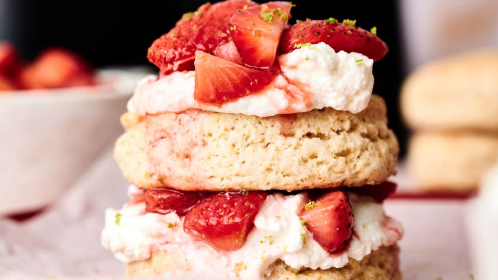 Two layers of biscuit with cream and sliced strawberries in between, topped with more strawberries and a sprinkle of green zest.