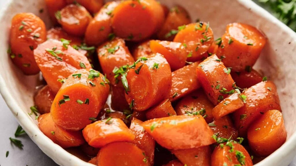 Close-up of glazed carrot slices garnished with chopped herbs in a white dish.
