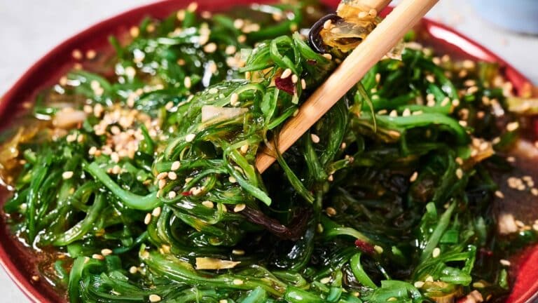 A plate of seaweed salad with sesame seeds, being lifted with chopsticks.