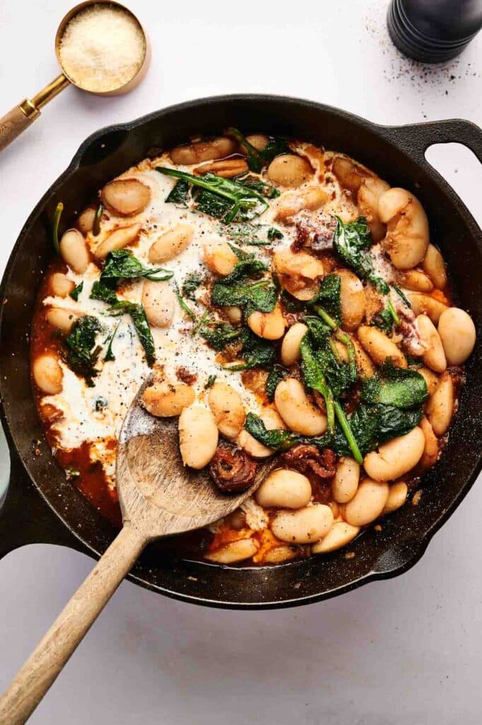 A cast iron skillet filled with "Marry Me Butter Beans," wilted spinach, and melted cheese, all mixed to perfection with a wooden spoon.