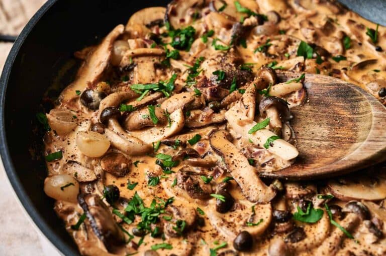 A skillet filled with luscious mushroom stroganoff, garnished with chopped parsley. A wooden spoon rests on the dish.