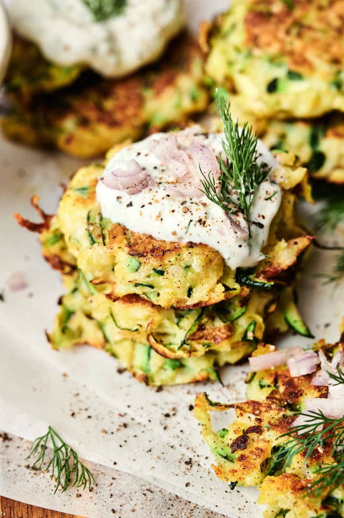 A stack of golden zucchini fritters topped with creamy sauce and garnished with fresh dill.