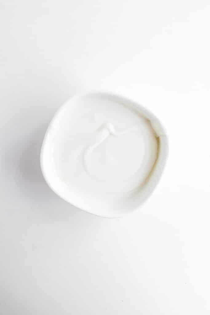 A small white bowl filled with plain yogurt sits on a white background—perfect for dipping your 4th of July Fruit Kabobs.