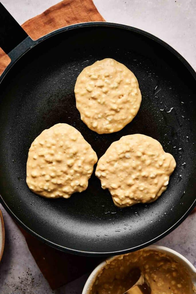 Three cottage cheese pancakes sizzling softly in a non-stick frying pan.