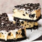 A slice of delicious Oreo cheesecake, adorned with crushed cookies and a drizzle of white icing, is being lifted from the plate. Oreo crumbs are playfully scattered around, completing this delightful scene.