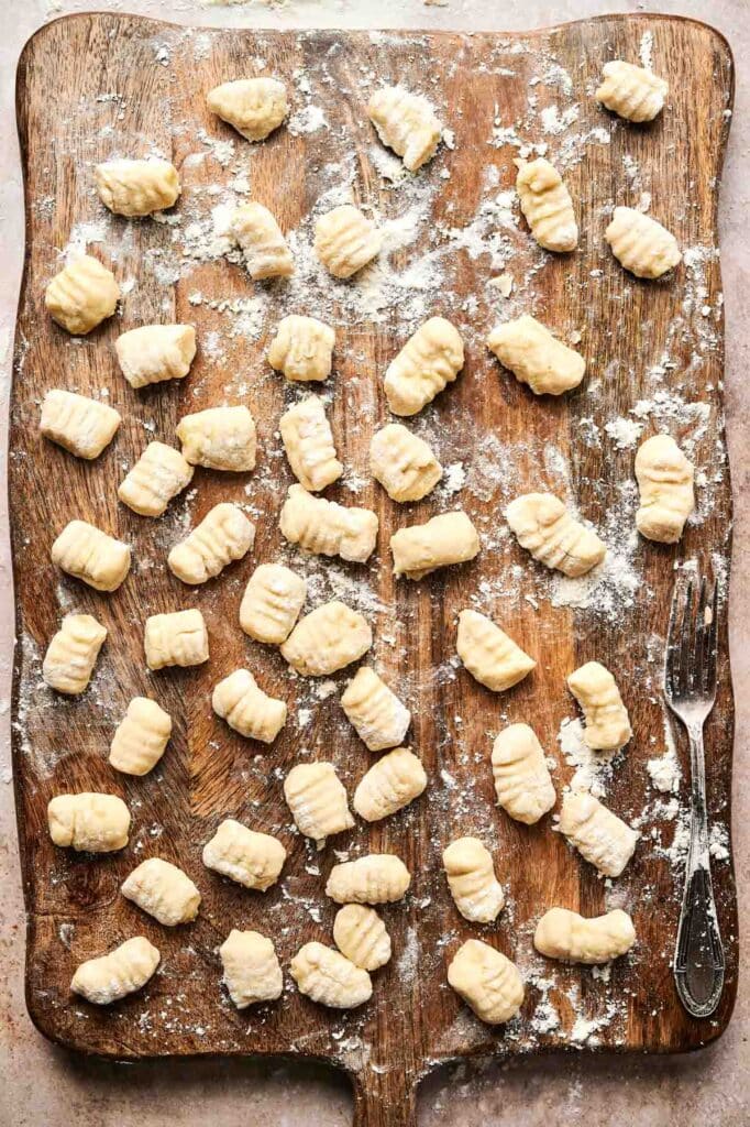 Uncooked gnocchi pieces are artfully scattered across a floured wooden cutting board, with a fork resting invitingly at the side.