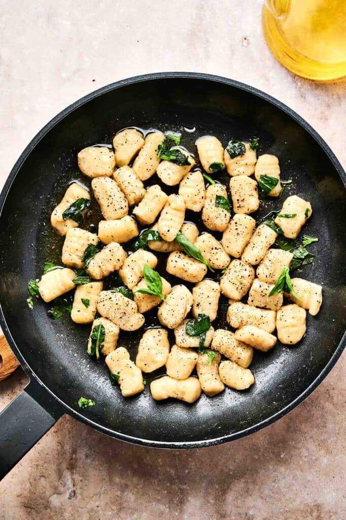 Sizzling gnocchi mingles with fresh herbs and a dash of pepper in a sleek black frying pan.