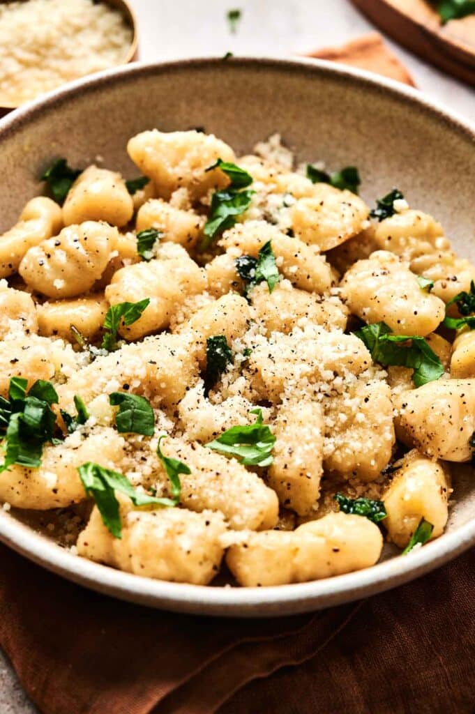 A delightful bowl of gnocchi garnished with grated cheese, black pepper, and fresh herbs.