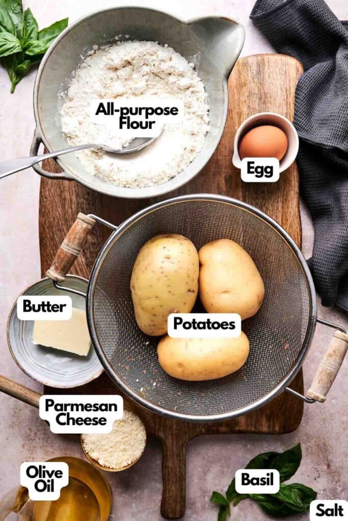 Gnocchi-making essentials gather elegantly on a wooden surface: flour, an egg, potatoes, butter, Parmesan cheese, olive oil, fresh basil, and a pinch of salt.
