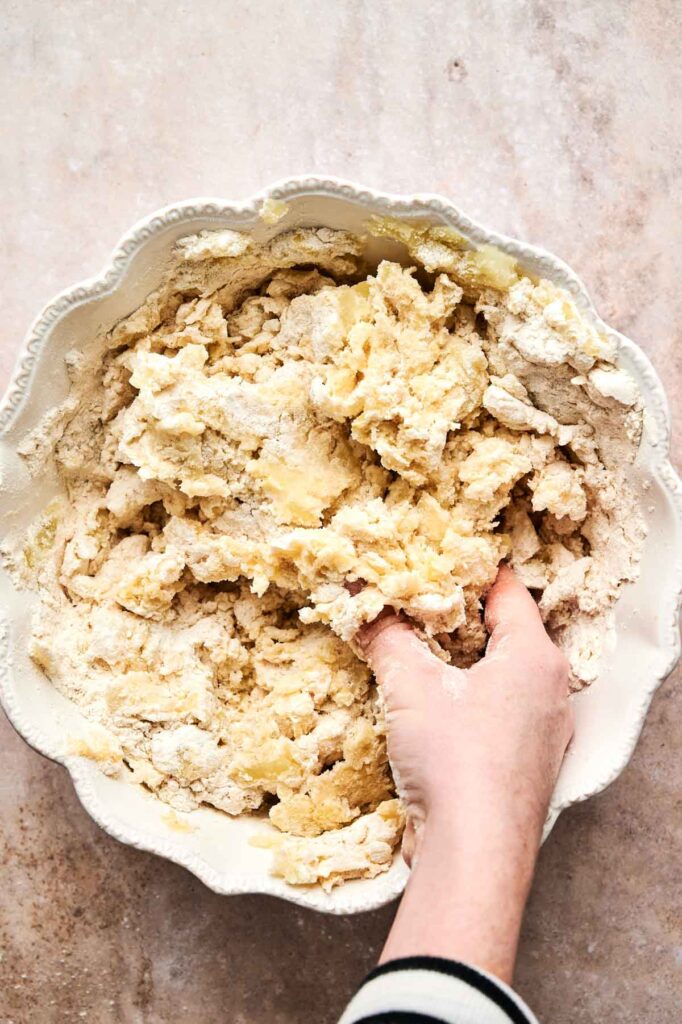 A hand expertly kneads dough for gnocchi in a white scalloped bowl on a marble surface.