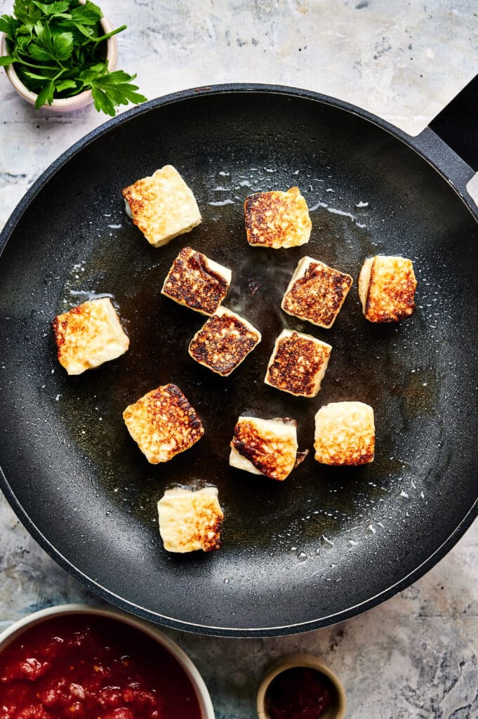 Cubes of paneer being fried in a pan, turning golden brown on top, reminiscent of halloumi crisping up for a delightful stroganoff.