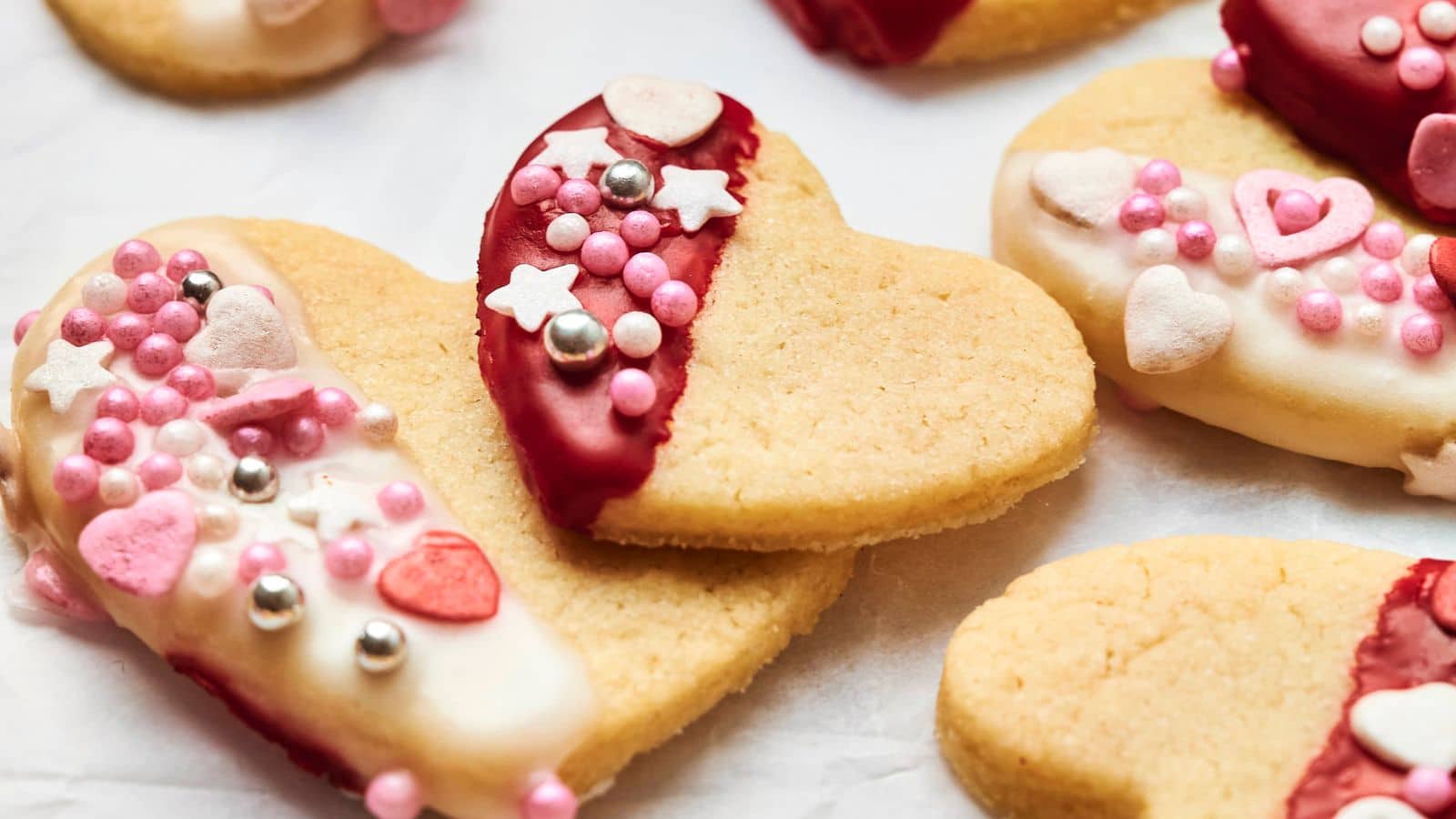 Heart-shaped cookies decorated with pink, white, and red icing and sprinkles, including stars and hearts, on a white surface.