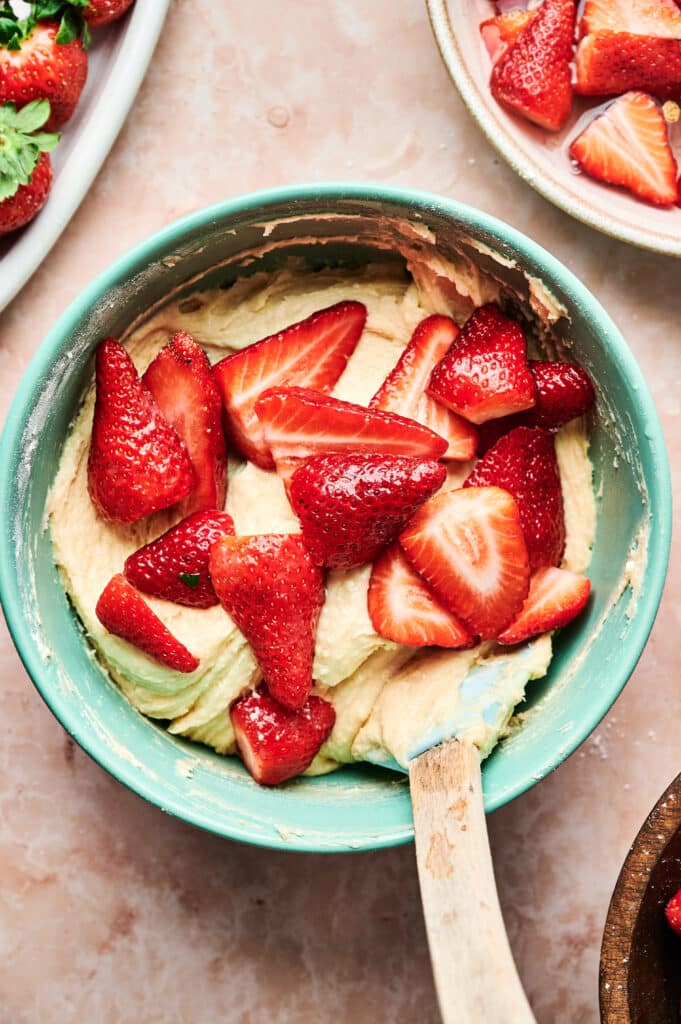 A mixing bowl brimming with strawberry cake batter, topped with sliced strawberries, and a spatula resting inside.