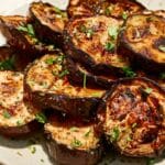 A plate of grilled eggplant slices garnished with chopped fresh herbs.