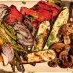 A platter of grilled vegetables, including asparagus, red onion, bell peppers, zucchini, and mushrooms, garnished with chopped herbs for a fresh touch. Enjoy this colorful medley of perfectly grilled vegetables.