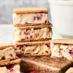 Ice cream sandwich delights with visible berry pieces are stacked on a wooden board, with a white bowl in the background.