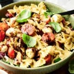 A bowl of Italian pasta salad with bowtie pasta, cherry tomatoes, mozzarella balls, fresh basil leaves, and a drizzle of balsamic dressing.