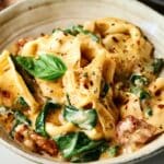 A bowl of creamy Marry Me Tortellini pasta with spinach, fresh basil, and tomato pieces, garnished with herbs and red pepper flakes.
