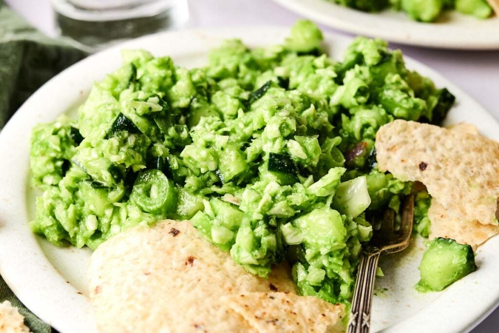Creamy green goddess salad is plated with crunchy tortilla chips and a fork.