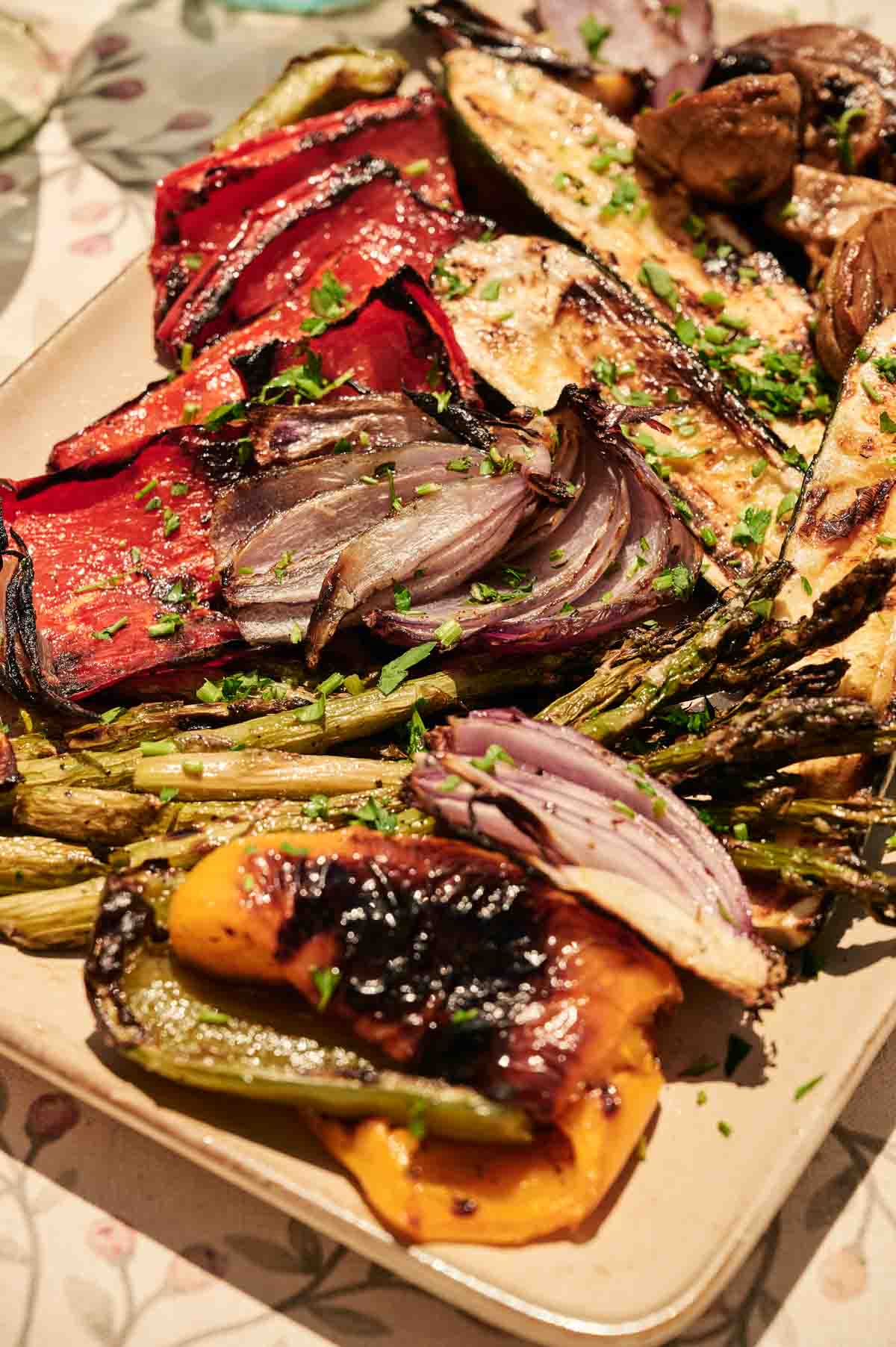 A plate of Grilled Vegetables featuring red onion, bell peppers, zucchini, and asparagus, all perfectly charred and garnished with chopped herbs.