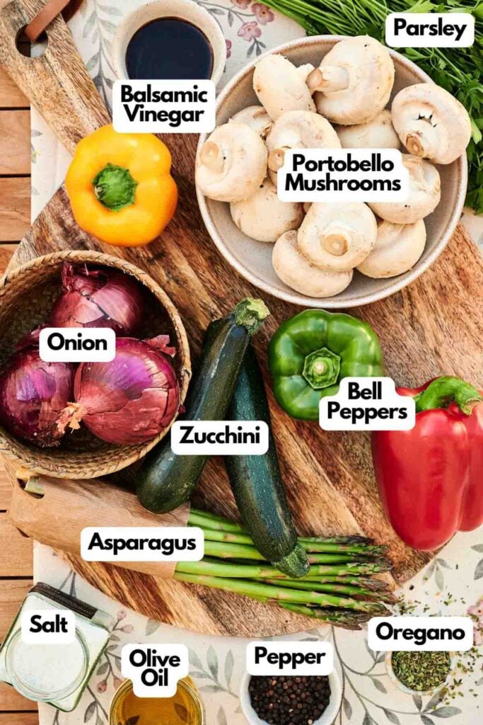 A variety of fresh vegetables and seasonings are arranged on a table, ready to be transformed into delicious grilled vegetables&mdash;featuring mushrooms, bell peppers, zucchini, onion, asparagus, parsley, oregano, salt, pepper, olive oil, and balsamic vinegar.