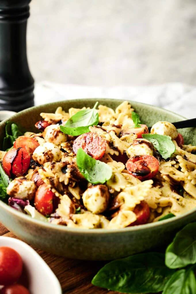 Bowl of Italian pasta salad featuring bowtie pasta, cherry tomatoes, mozzarella balls, basil leaves, and a drizzle of balsamic glaze.