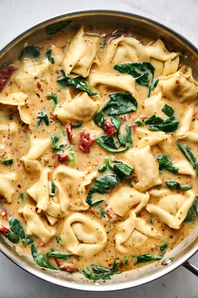 A skillet filled with creamy Marry Me Tortellini pasta, spinach, and sun-dried tomatoes in a rich, flavorful sauce.