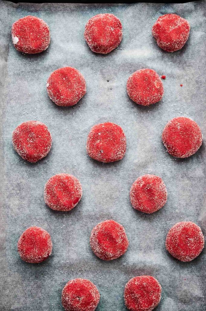 Rows of red, sugar-coated strawberry cookies arranged on a parchment-lined baking tray, ready for baking.