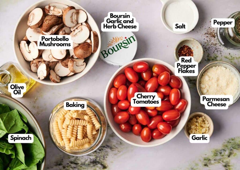 A top-down view of ingredients labeled for a recipe: portobello mushrooms, Boursin cheese, salt, pepper, cherry tomatoes, parmesan, garlic, red pepper flakes, olive oil, spinach, and pasta.