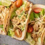 Three soft tortillas filled with lettuce, sautéed mushrooms, shredded cheese, and cherry tomato halves create delicious mushroom tacos, served with a lime wedge on the side.
