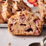 A close-up of a sliced strawberry bread loaf with visible chunks of strawberries and a light drizzle of icing on top, capturing the moist texture and sweet flavors of homemade strawberry bread.