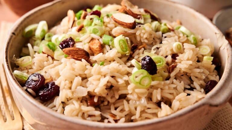 A bowl of cooked rice topped with sliced green onions, almonds, and dried cranberries.
