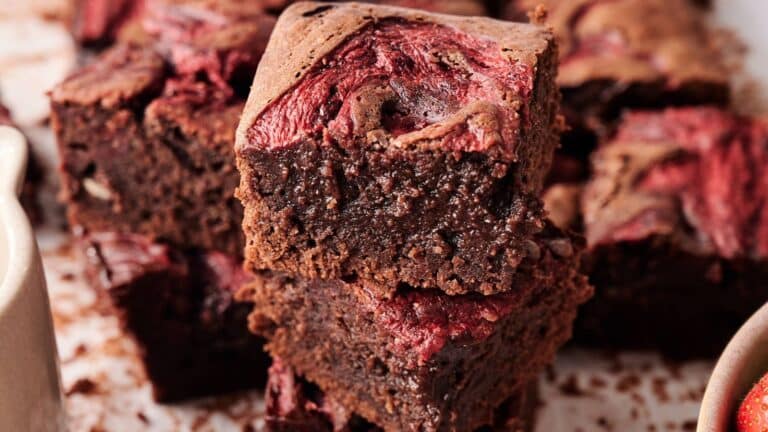 Two thick, fudgy chocolate brownies with visible swirls of red berry puree stacked on top of each other, surrounded by more brownies in the background.
