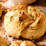 Close-up of Air Fryer Garlic Knots topped with herbs and seasoning, resting on a parchment-lined surface.