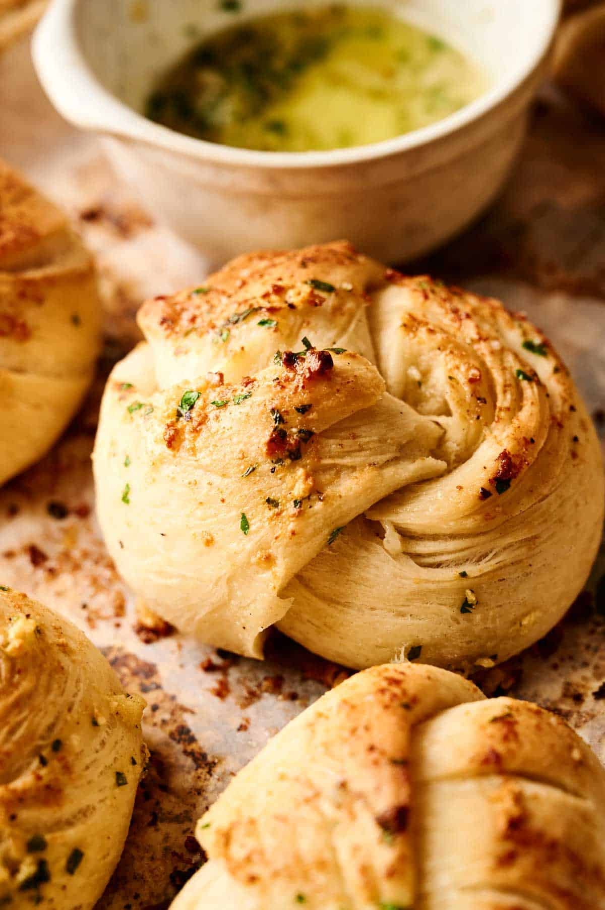 A close-up of golden-brown Air Fryer Garlic Knots sprinkled with herbs, with a small bowl of garlic butter sauce in the background.