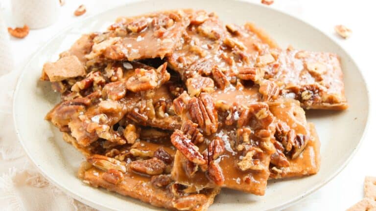 A plate of pecan toffee brittle pieces topped with chopped pecans and a caramelized sugar coating.