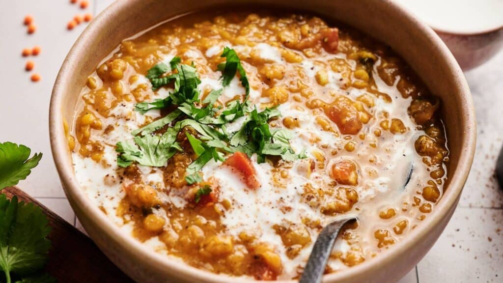 A bowl of lentil curry garnished with fresh cilantro and a swirl of cream, with a spoon in the bowl.