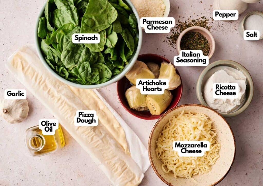 Top-down view of ingredients for a Spinach Pizza, featuring spinach, pizza dough, garlic, olive oil, artichoke hearts, cheeses, Italian seasoning, salt, and pepper.