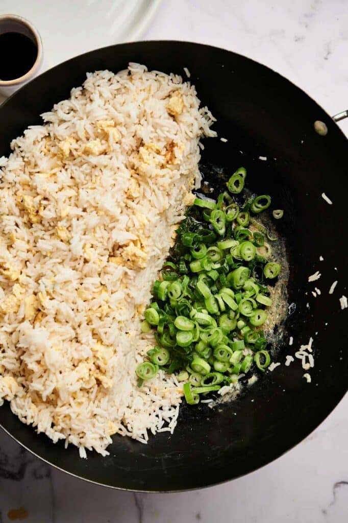 Egg Fried Rice in progress: cooked rice, scrambled eggs, and sliced green onions in a black wok, ready to be mixed together on a marble countertop.