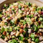 A close-up of a vibrant Celery Salad with chopped celery, apples, red onions, parsley, and almonds served in a beige bowl.