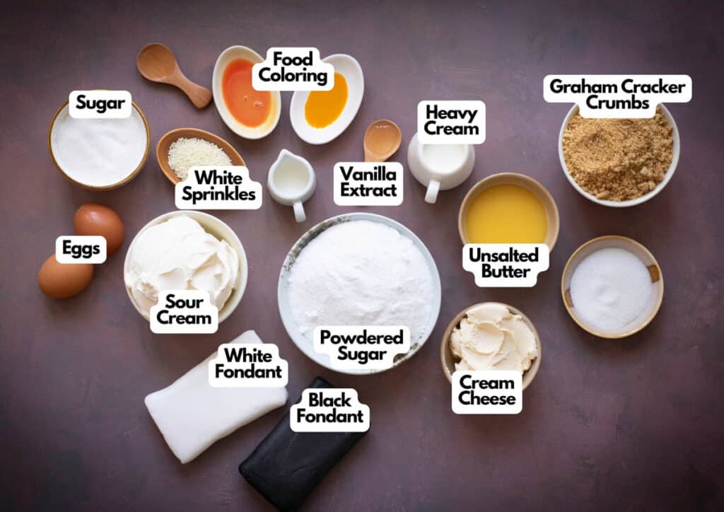 Various baking ingredients, including sugar, eggs, sour cream, white and black fondant, powdered sugar, food coloring, vanilla extract, heavy cream, butter, cream cheese, crumbs, and sprinkles—perfect for Halloween Candy Corn Mini Cheesecakes.