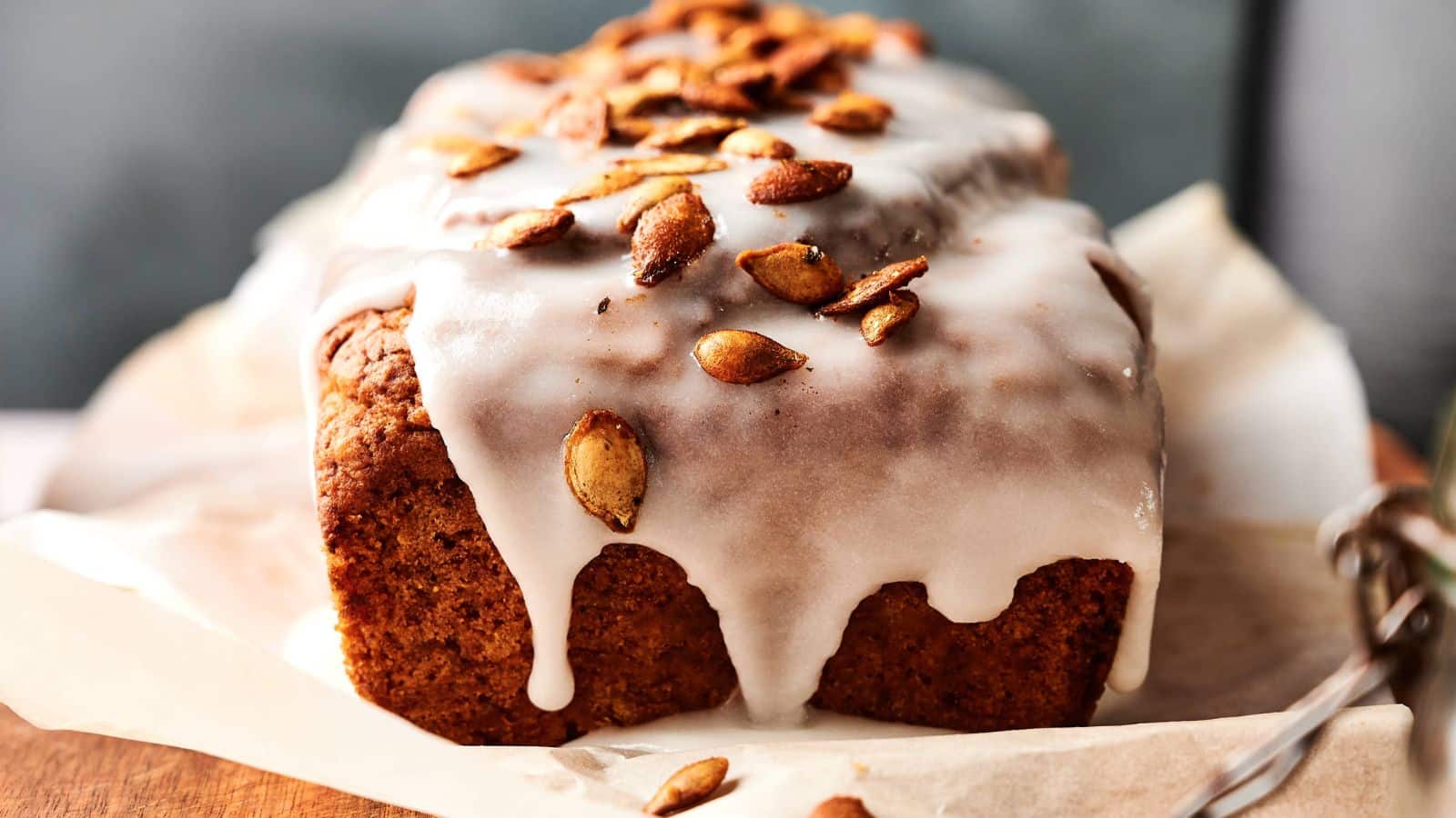 A close-up of a sliced pumpkin loaf cake with white icing and pumpkin seeds on top, showing its moist and crumbly texture.