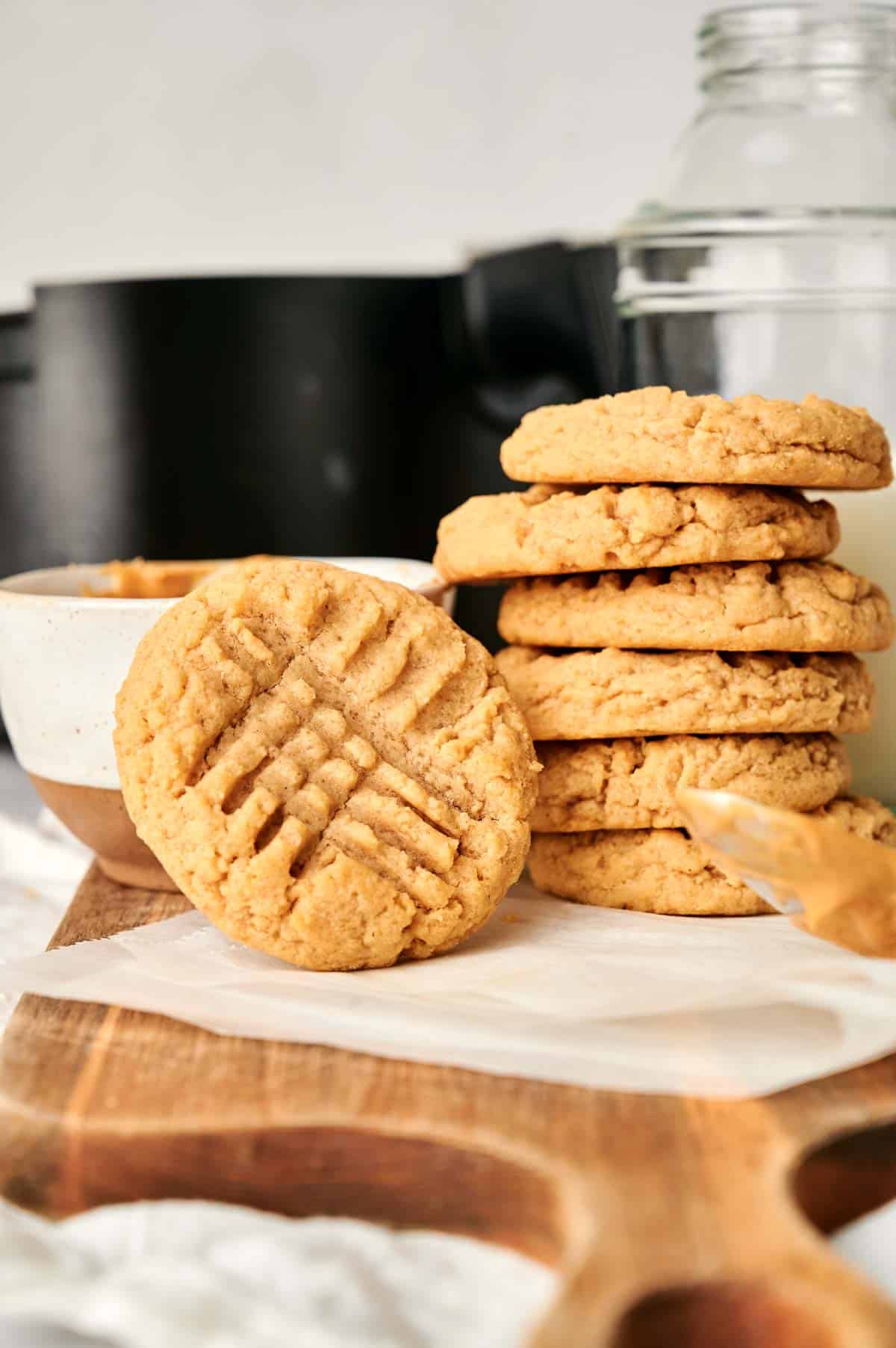 A stack of Air Fryer Peanut Butter Cookies sits next to a glass jar of milk, with one cookie in front displaying a classic crisscross fork pattern.