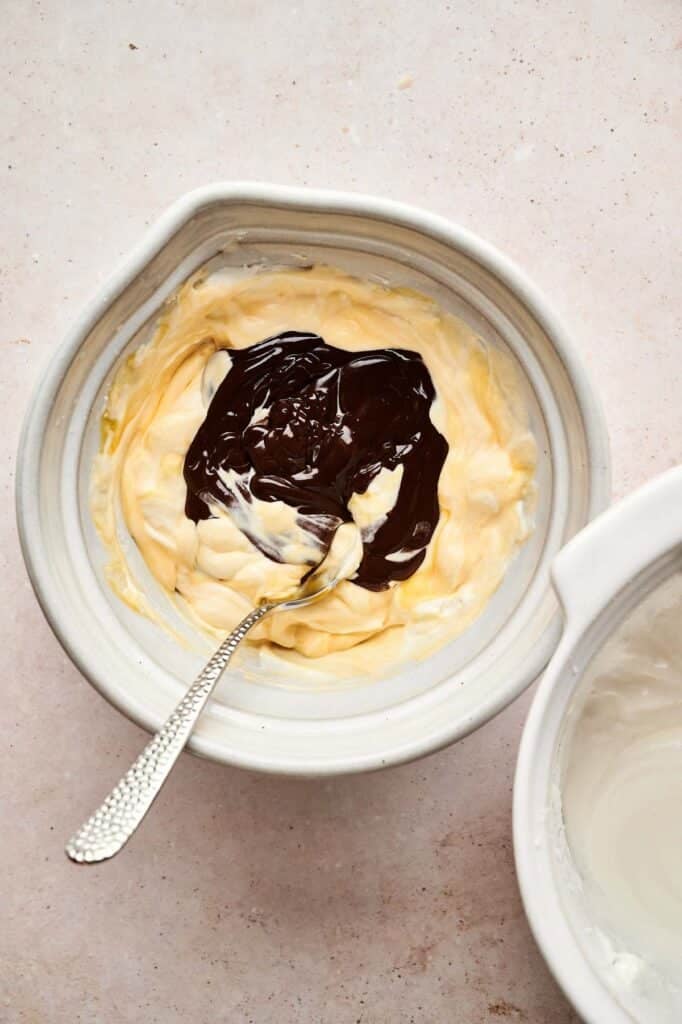 A bowl containing a mixture of yellow cream and melted chocolate with a spoon resting inside, perfect for creating rich Chocolate Mousse.