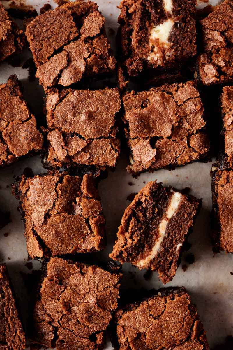 A close-up of several cut cream cheese brownies with a crumbly top, some pieces revealing a luscious white filling inside.