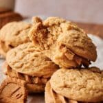 A close-up of several Biscoff Sandwich Cookies and peanut butter cookies, with one cookie on top showing a bite taken out, revealing a soft, crumbly texture inside.