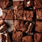 A batch of Cream Cheese Brownies, some with a visible cream cheese layer, are cut into squares and arranged on a parchment-lined surface.