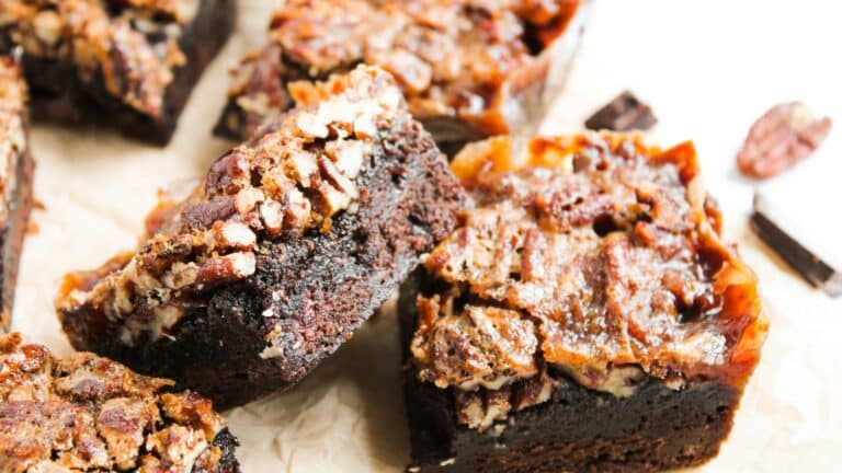 Close-up of several pecan-topped brownies on parchment paper, showing their rich, dense texture and nutty topping.