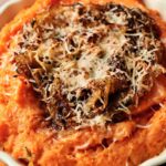 Mashed sweet potatoes baked to perfection, topped with caramelized onions and shredded cheese in a round baking dish.